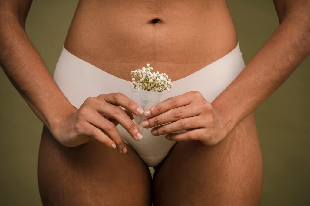 Photo du bas ventre d'une femme en culotte blanche. Elle se tient dans ses mains une cup avec des fleurs dedans.